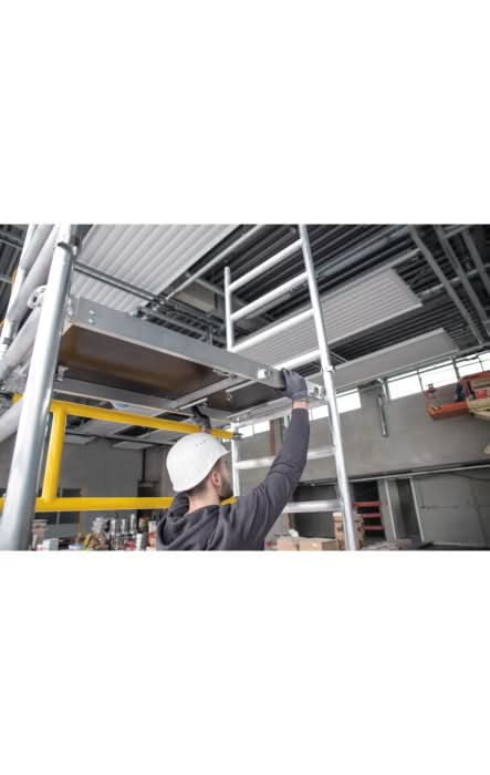 Ein arbeiter in weißem helm montiert das metallische ein-personen-gerüst munk flexxtower in einem lagerhaus
