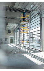 Gelb-silbernes MUNK FlexxTower Ein-Personen-Gerüst mit modularem Gerüstpodest und Arbeiter darauf