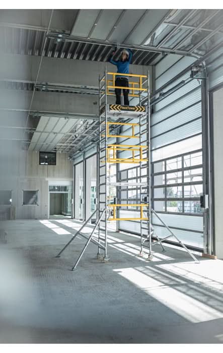 Gelb-silbernes MUNK FlexxTower Ein-Personen-Gerüst mit modularem Gerüstpodest und Arbeiter darauf