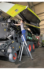 Munk stufen-stehleiter einseitig begehbar mit clip-step relax mit hellgrün-schwarzer landmaschine und gelbem warnschild auf geöffneter haube