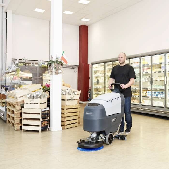 Graue und weiße Nilfisk scheuersaugmaschine sc401 b mit blauem bürstenkopf und batterie für industrielle bodenreinigung